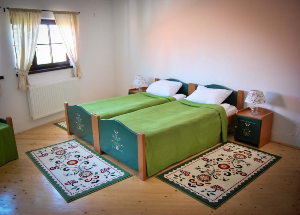 Dormitor cu două paturi verzi și covorașe cu motive florale.
