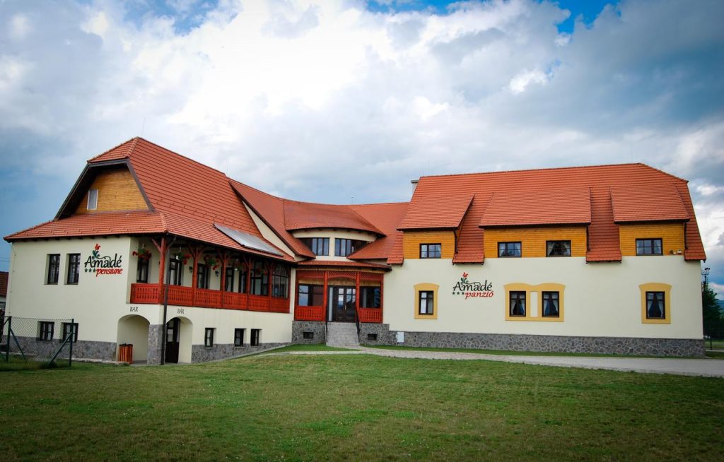 Clădire cu acoperiș roșu, balcoane și gazon în față.
