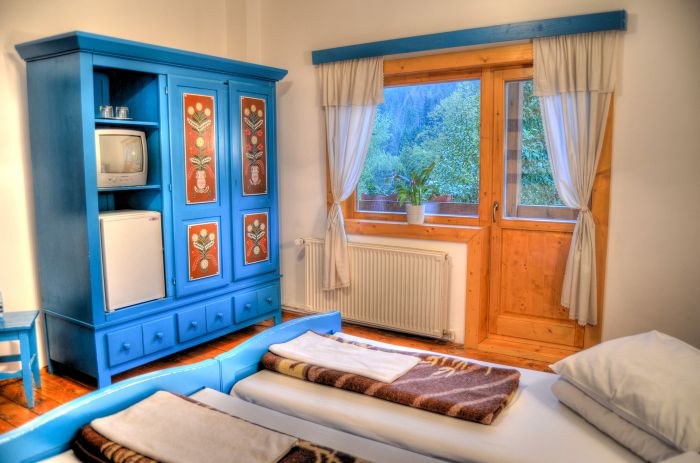 Dormitor cu pat și dulap albastru pictat, lângă o fereastră.