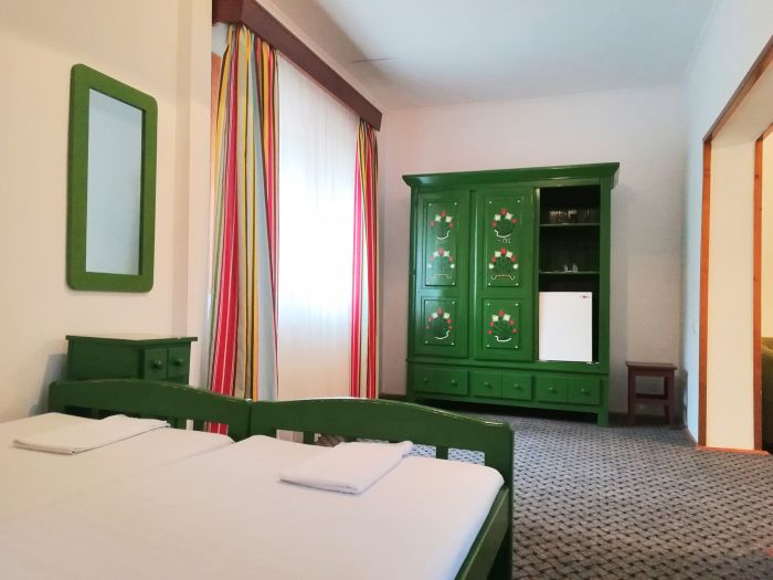 Dormitor cu pat și dulap verde, lângă perdele dungate.