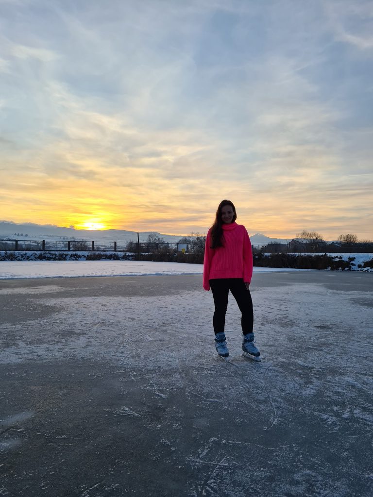 Femeie în geacă roz pe gheață, în lumina apusului.