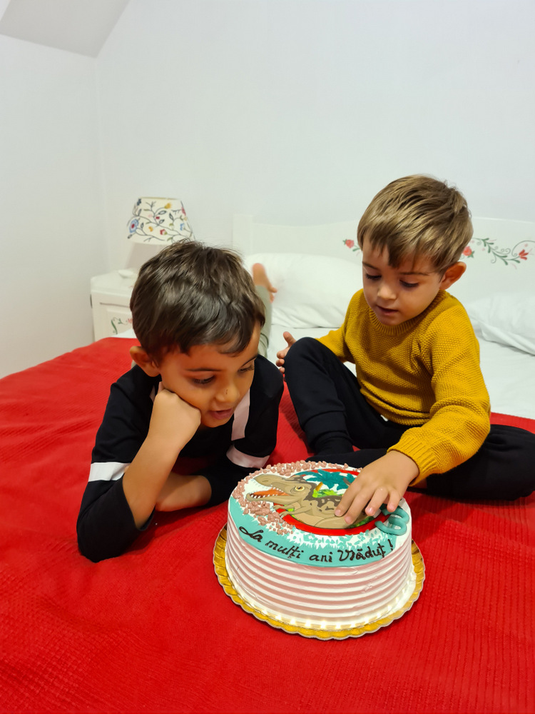 Doi copii lângă un tort colorat, pe un pat.