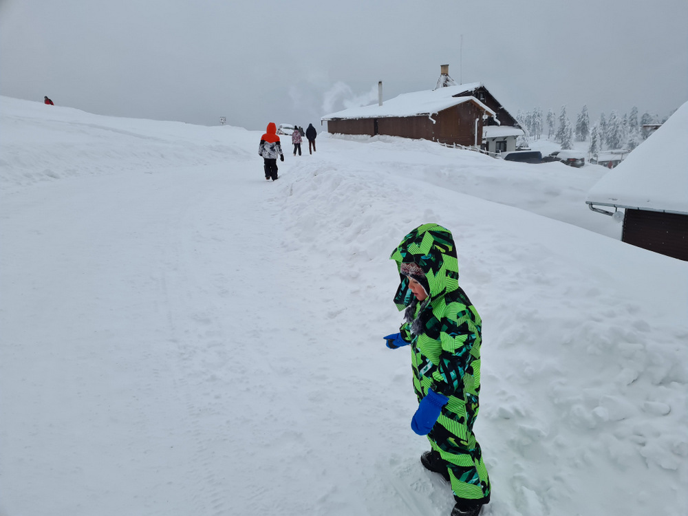 Copil cu snowboard lângă o cabană înzăpezită