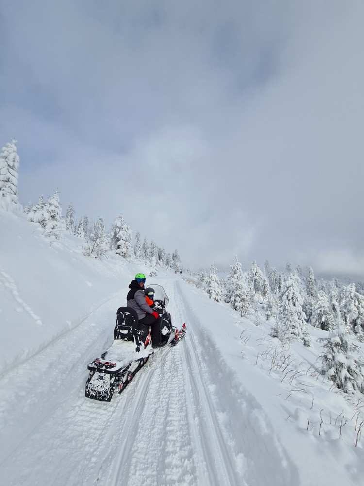 Snowmobile și persoane pe un versant acoperit de zăpadă