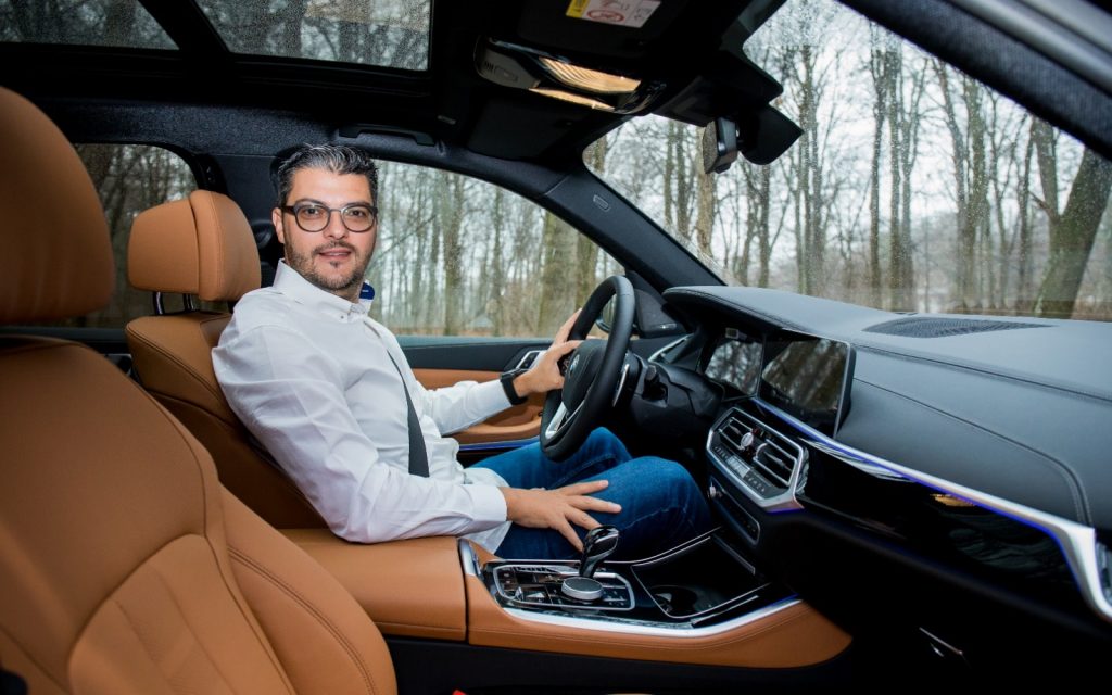 Bărbat cu ochelari la volanul unei mașini cu interior maro.