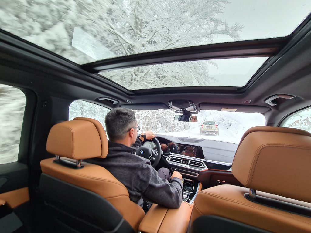 Interior de mașină cu plafon panoramic și pădure înzăpezită deasupra.