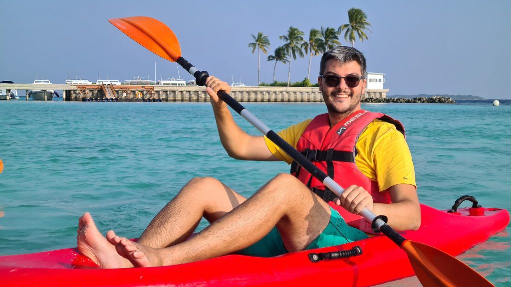 Bărbat cu vestă de salvare și padelă într-un caiac roșu.