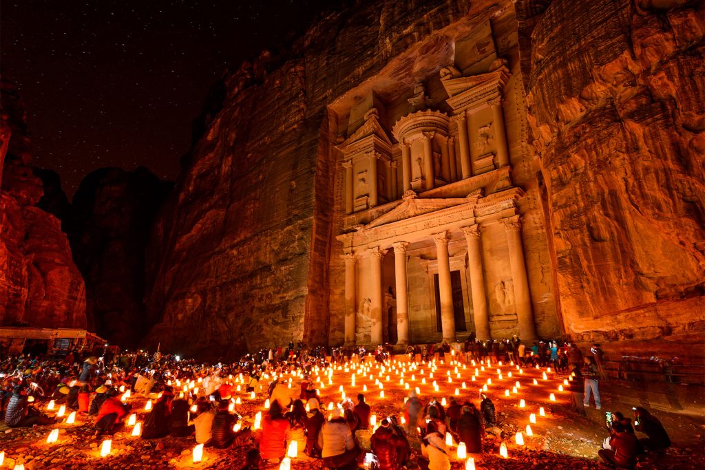 Fațadă sculptată în stâncă, luminată de numeroase lumânări.