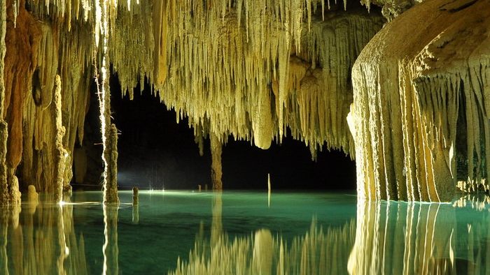 Stalactite lungi deasupra apei limpezi dintr-o peșteră.