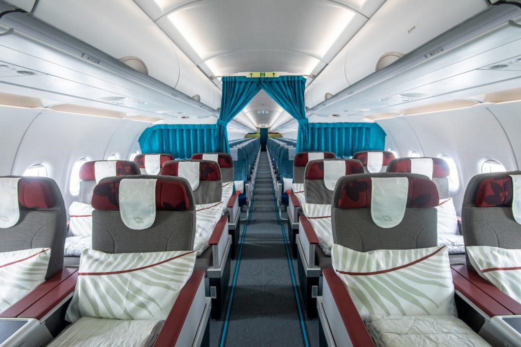 Interior de avion cu rânduri de scaune și perdele turcoaz.