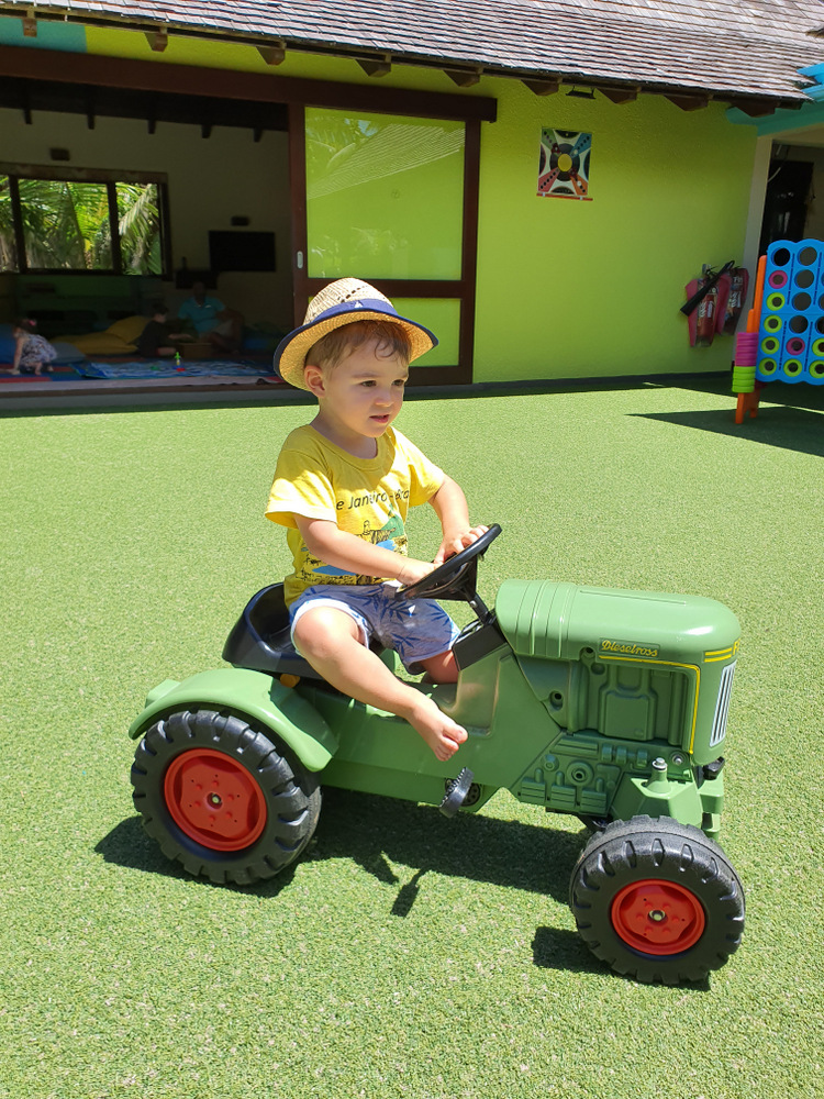 Copil cu pălărie pe un tractor verde de jucărie.