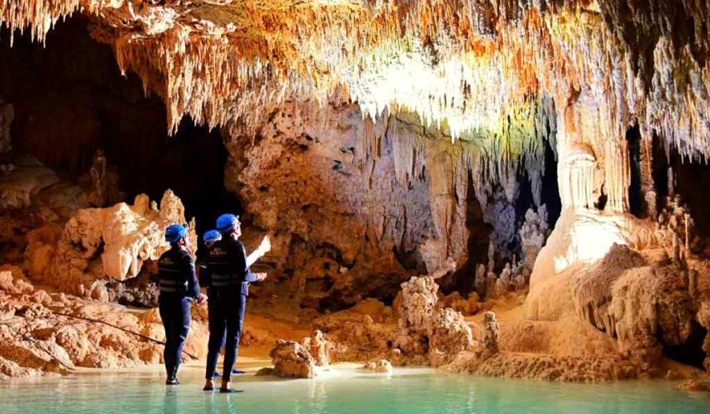 Două persoane cu căști într-o peșteră luminată cu stalactite.
