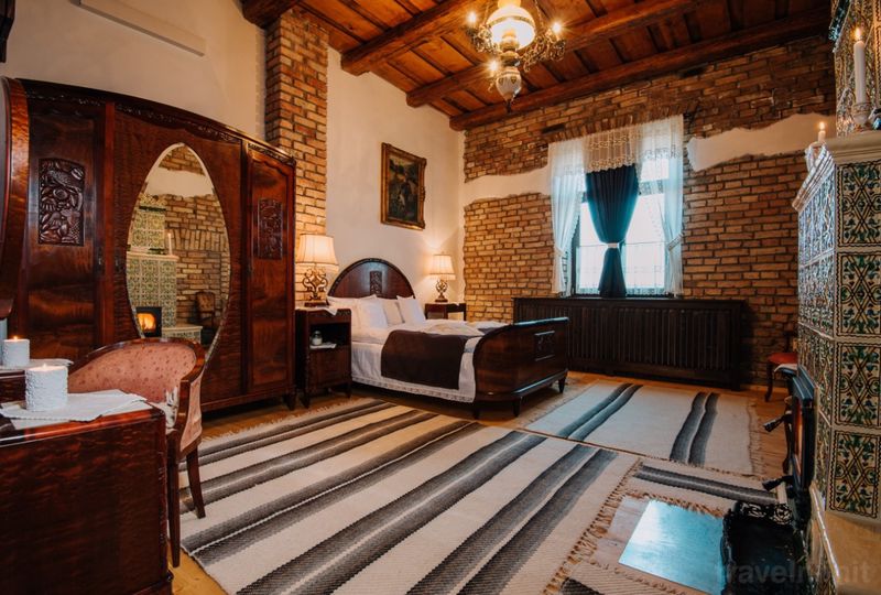Dormitor rustic cu pat dublu, cărămidă aparentă și grinzi.