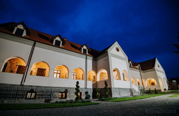 Clădire albă cu ferestre arcuite iluminate, la lăsarea nopții.
