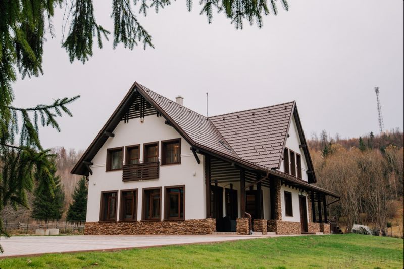 Casă albă cu acoperiș înclinat, lângă gazon și pădure.