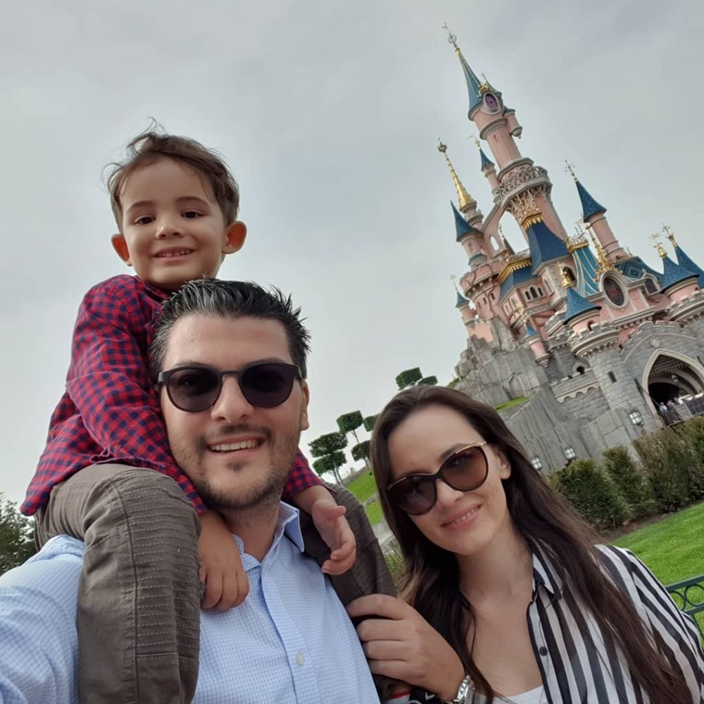 Bărbat cu copil pe umeri și femeie, lângă un castel.