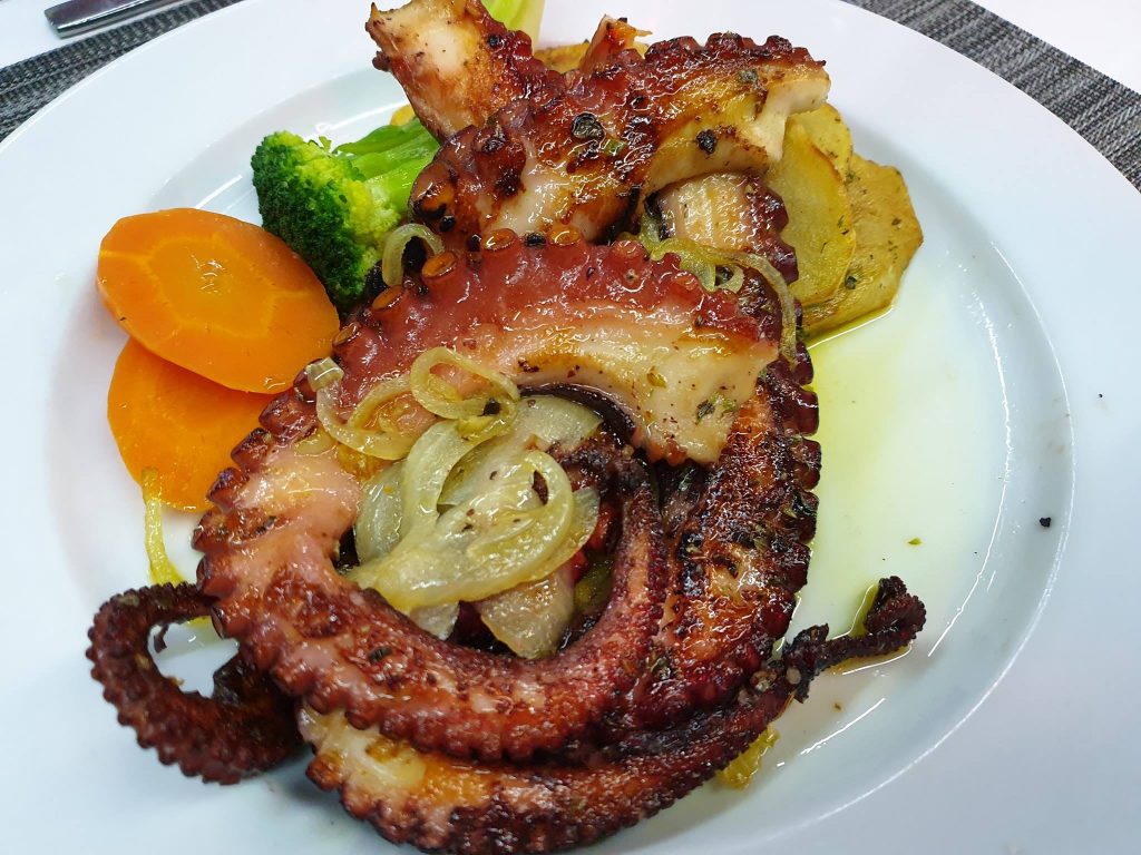 Tentacule rumenite cu ceapă, cartofi și legume pe farfurie.
