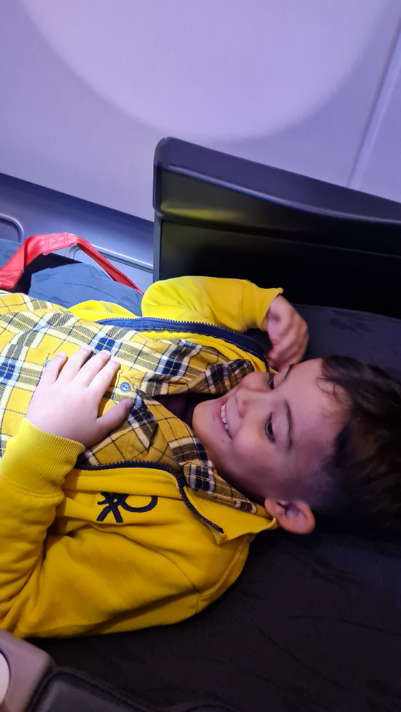 Copil adormit pe un scaun de avion, cu centura prinsă.