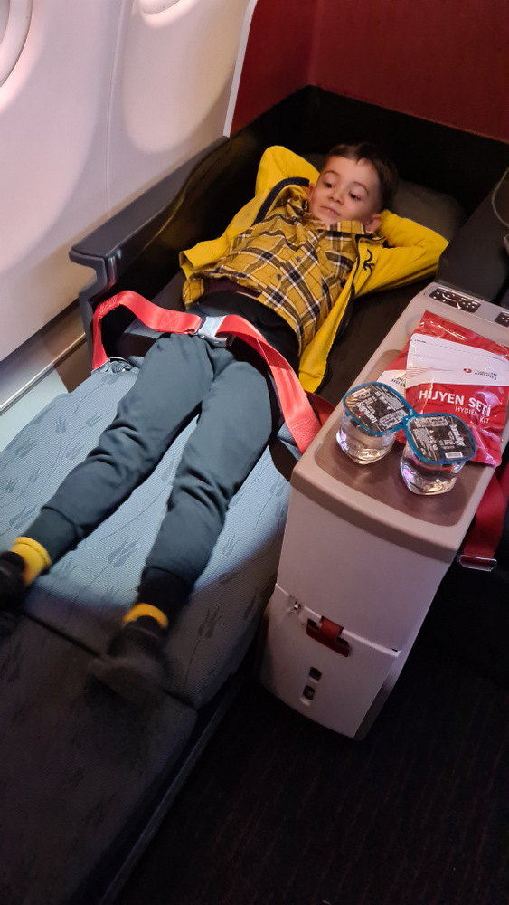 Copil în cămașă galbenă întins într-un fotoliu de avion.
