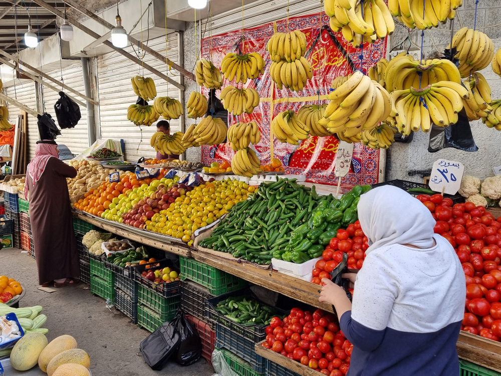 Tarabă cu banane suspendate și legume în lăzi.