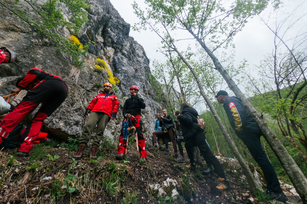 Grup cu căști și hamuri la baza unui perete stâncos.