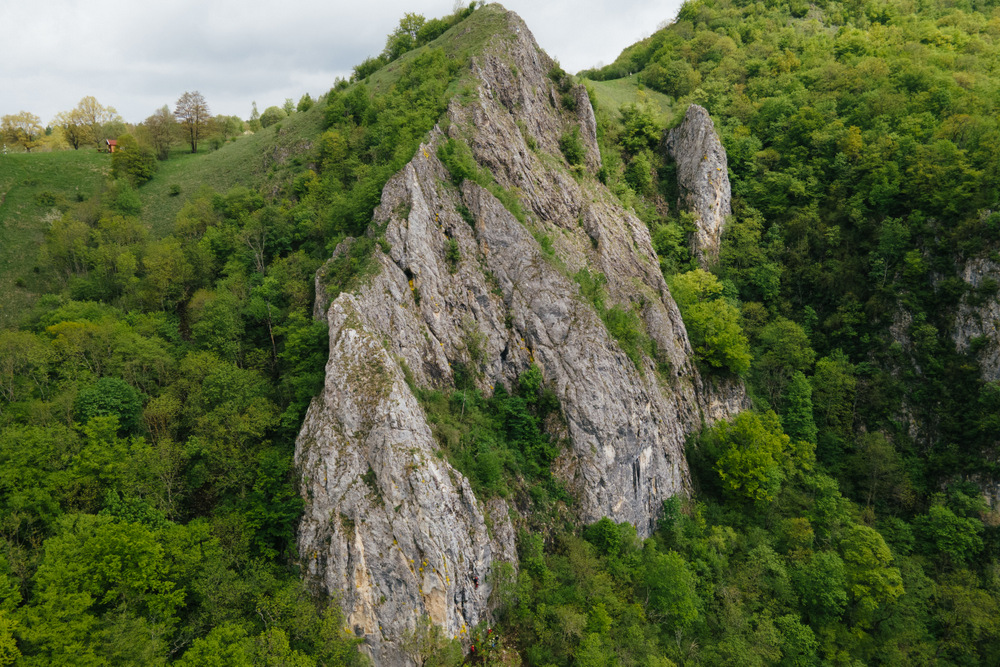 Creastă stâncoasă ascuțită înconjurată de versanți acoperiți cu pădure.