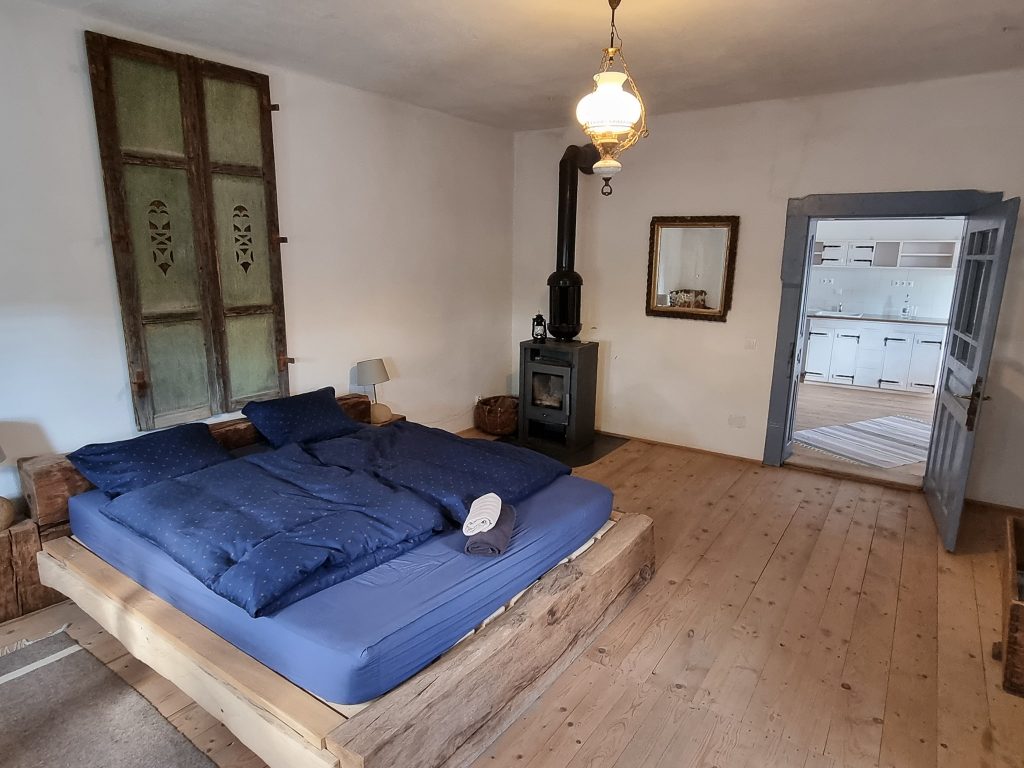 Dormitor rustic cu pat albastru și sobă neagră.