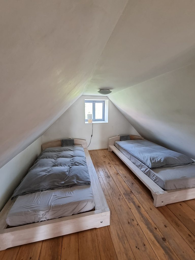 Două paturi într-o mansardă îngustă cu fereastră mică.