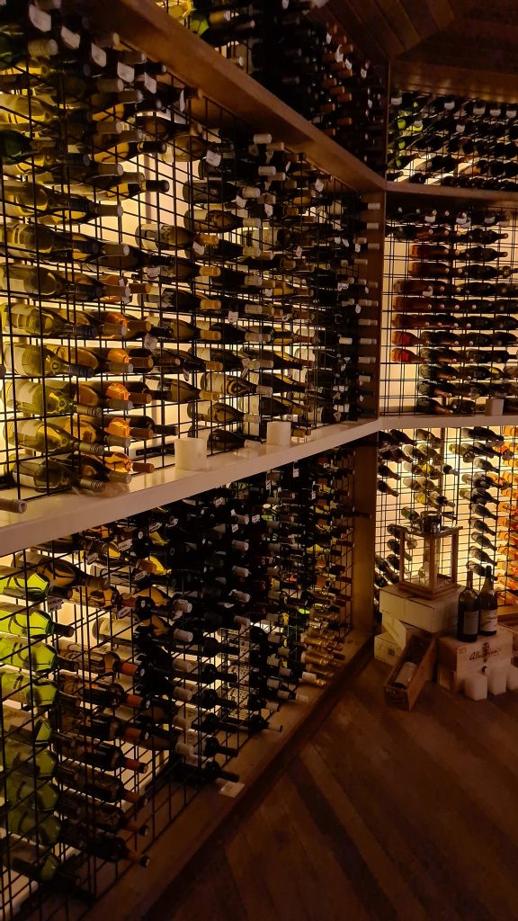 Rafturi cu sticle de vin într-o încăpere slab luminată.