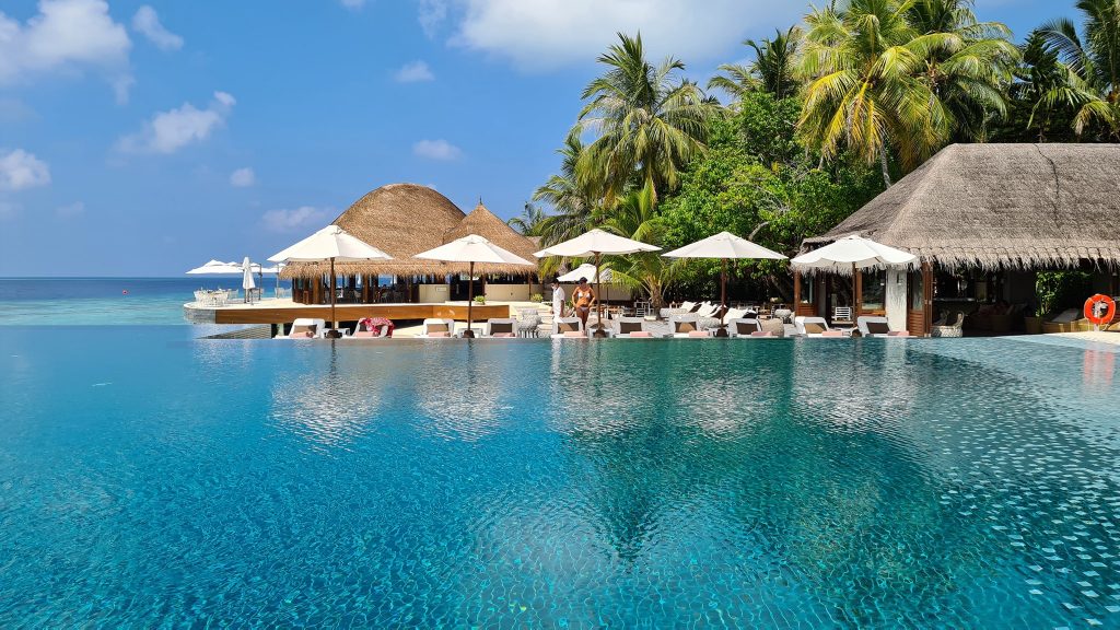 Piscină albastră cu pavilioane și palmieri pe margine.