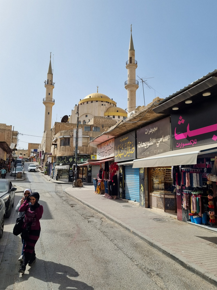 Stradă comercială cu pietoni și o moschee cu minarete în fundal.