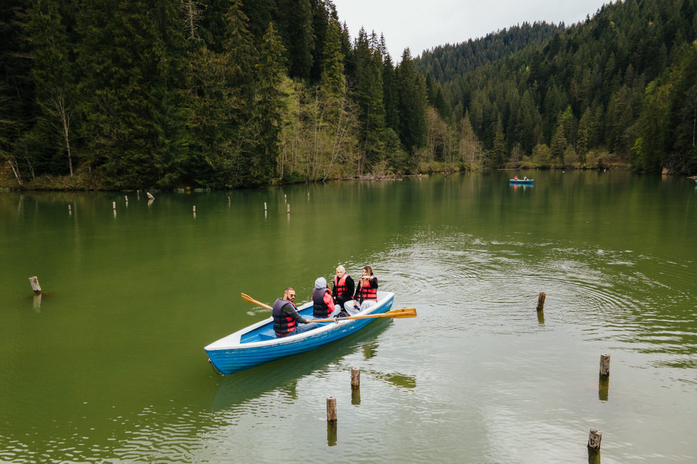 Persoane într-o barcă pe Lacul Roșu, lângă pădure