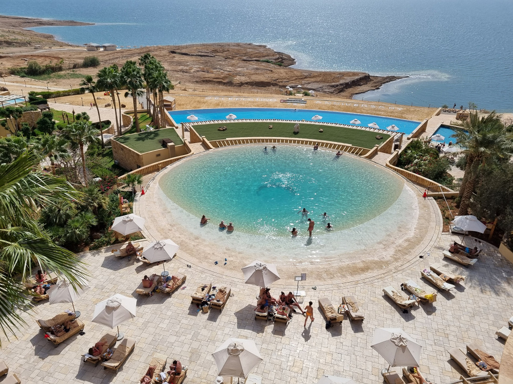 Piscină rotundă cu șezlonguri, deasupra unui țărm stâncos.