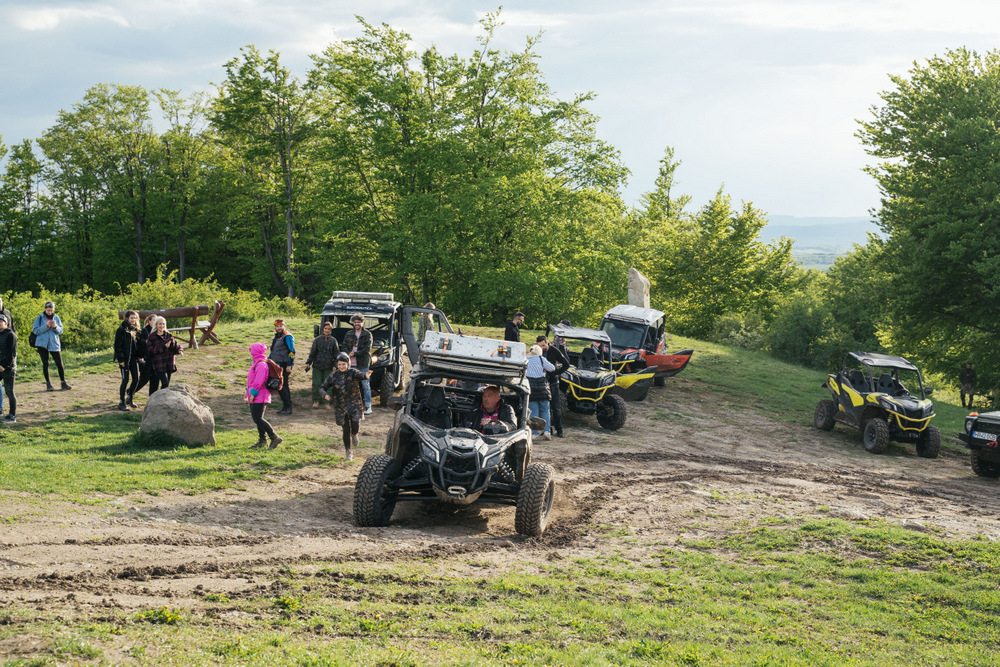 Persoane și vehicule de teren într-o poiană lângă pădure.