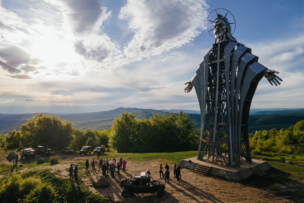 Statuie metalică monumentală, văzută dinspre o pajiște