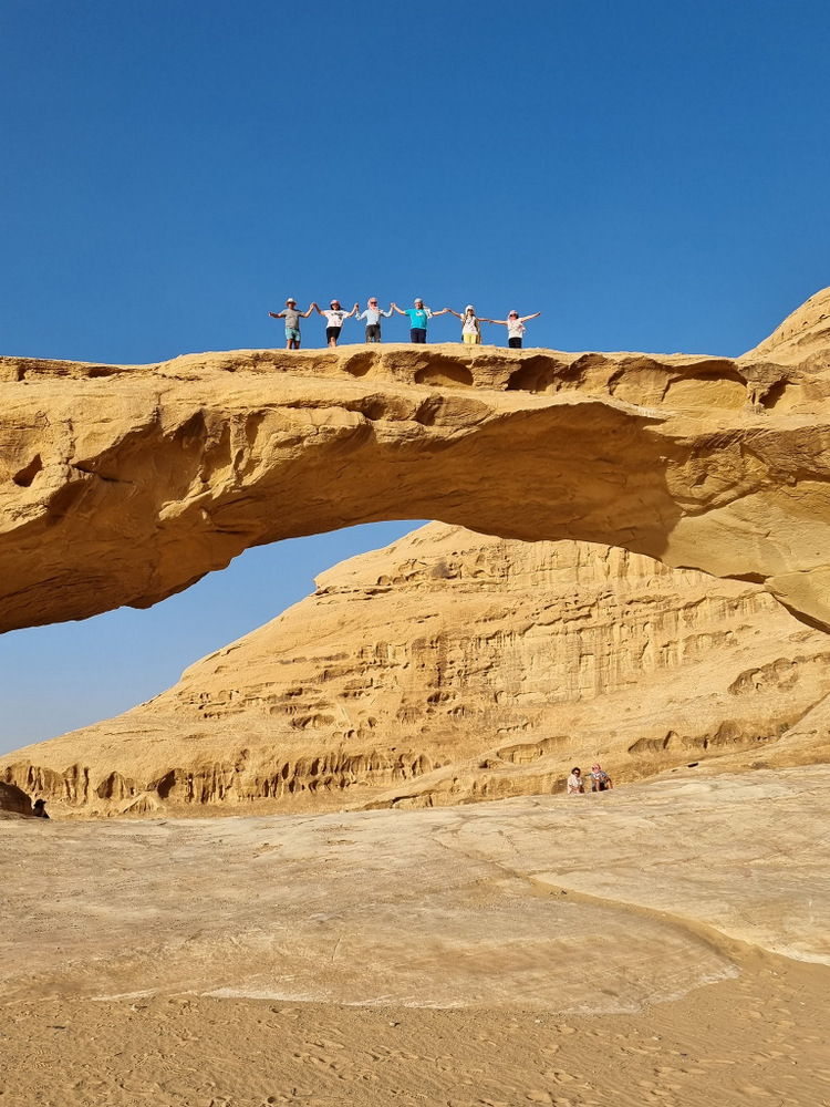 Persoane pe un arc natural de piatră în deșert.