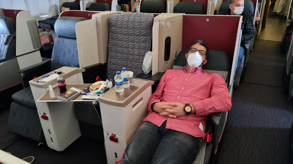 Bărbat cu mască întins într-un fotoliu rabatat de avion.