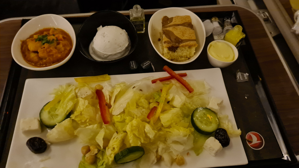 Tavă cu salată, pâine și boluri cu mâncare.