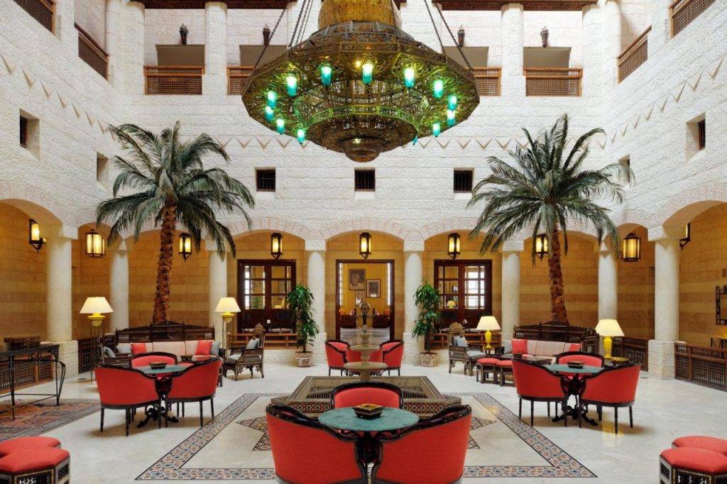 Atrium cu candelabru mare, palmieri și mese rotunde.