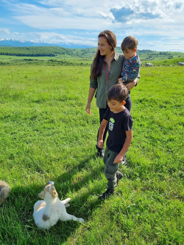 Femeie și copii într-o pajiște lângă un câine alb.