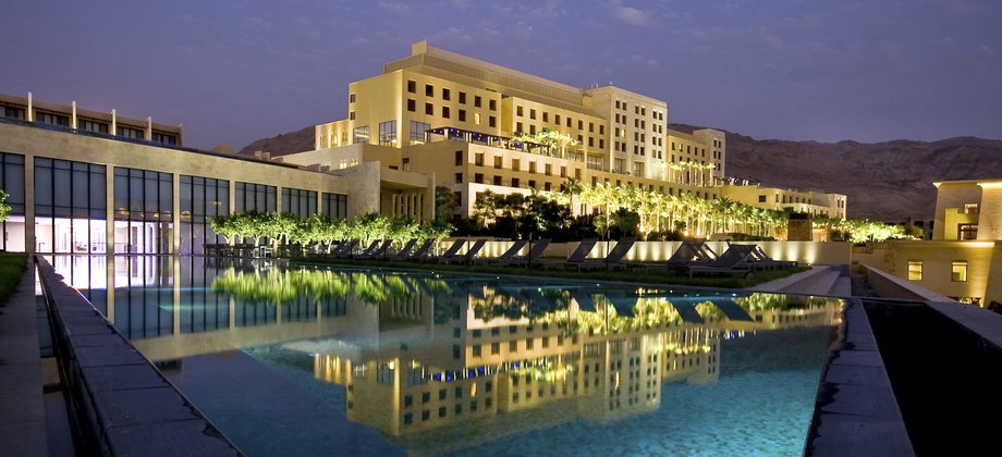 Clădire luminată noaptea, reflectată într-o piscină mare.