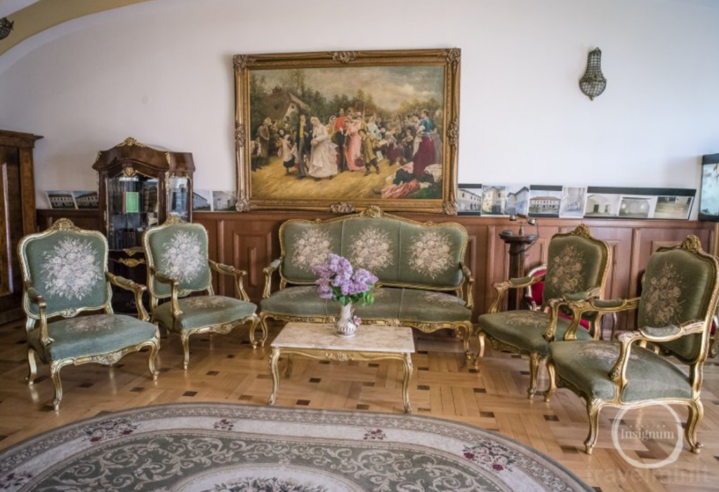 Salon cu mobilier sculptat, tapițerie verde și tablou mare.