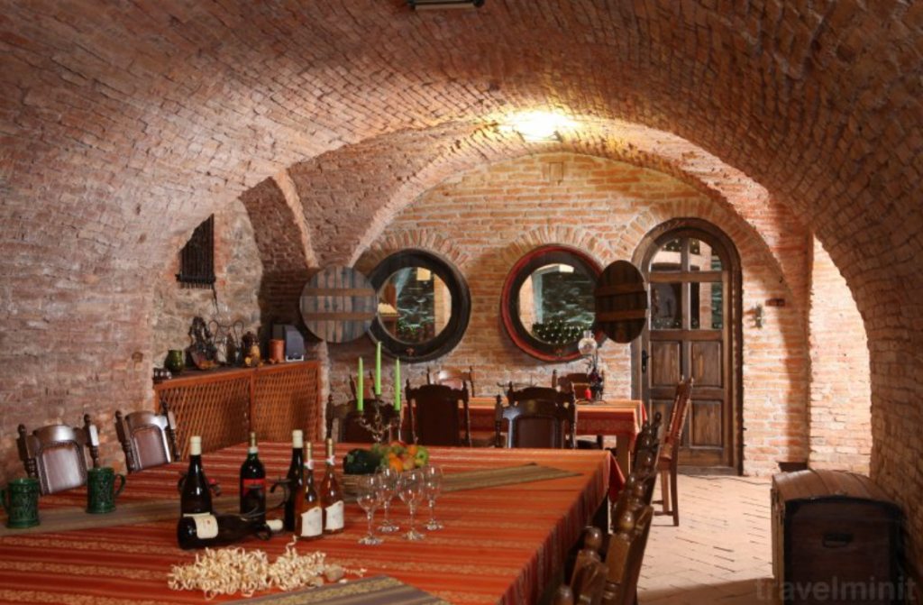 Pivniță boltită din cărămidă, cu masă și sticle de vin.