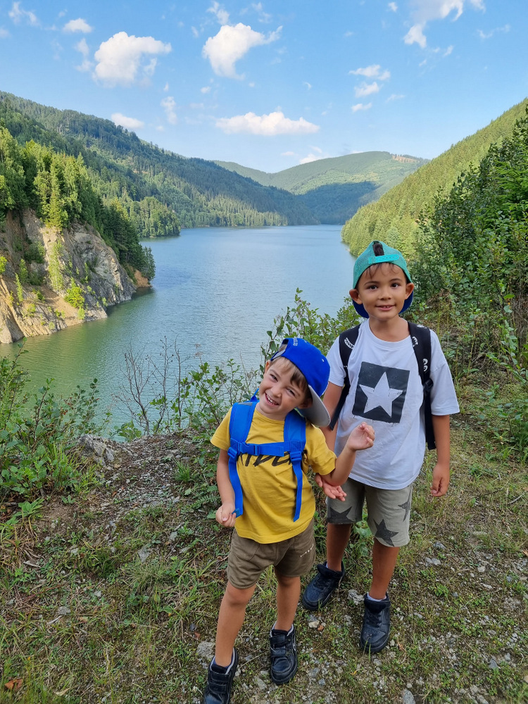 Doi copii la un punct de belvedere deasupra unui lac montan.