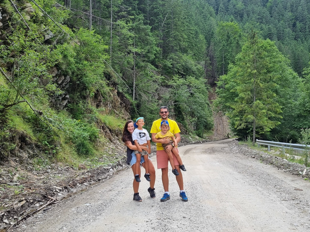 Doi copii pe un drum montan, între versanți împăduriți.
