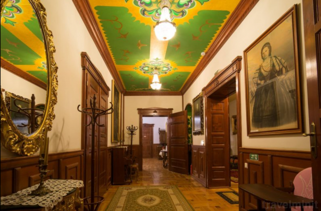 Coridor cu lambriuri, tablouri și plafon pictat în culori vii.