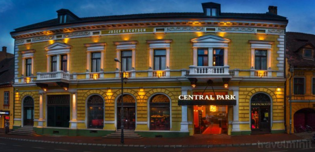Fațadă galbenă iluminată seara, cu intrare centrală.