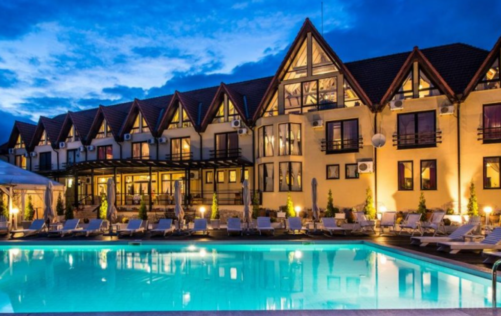 Clădire cu frontoane iluminate lângă o piscină nocturnă.