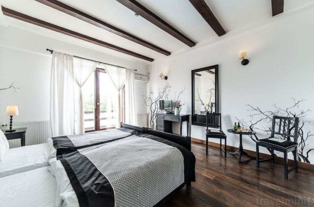 Dormitor alb cu grinzi întunecate și mobilier negru.