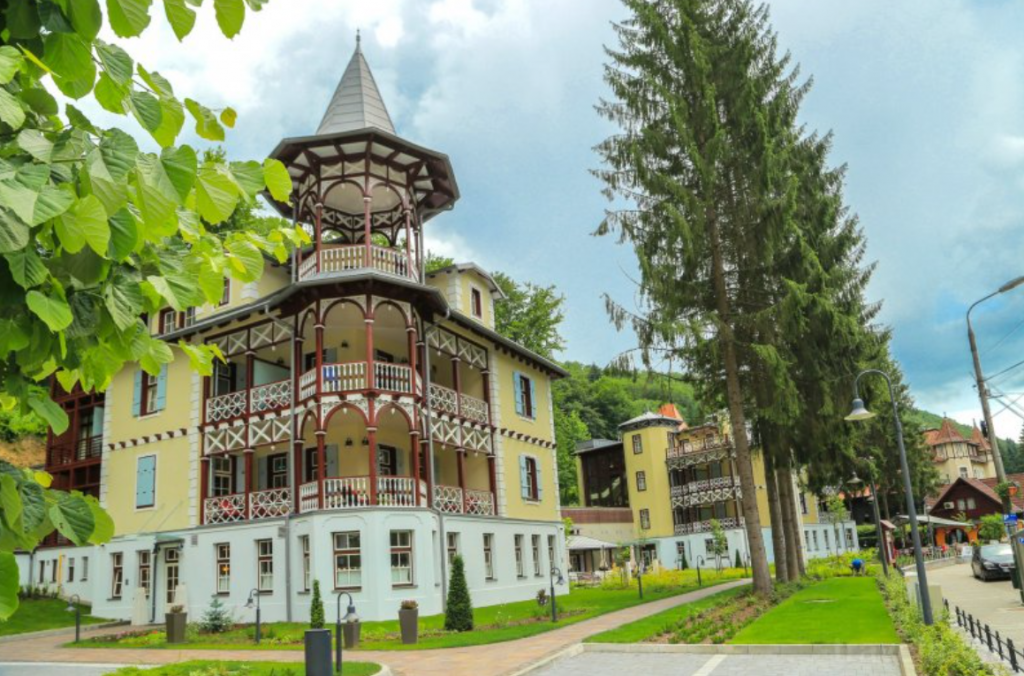 Clădire cu turn și balcoane din lemn între arbori.